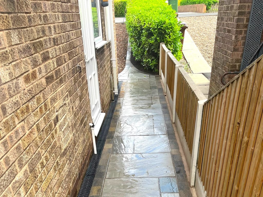 Sandstone side path running between a house wall and a close boarded fence