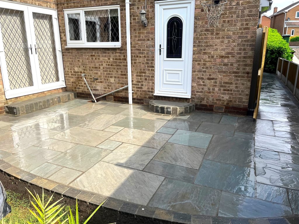 Sandstone paving at a white front door with a dark sett border