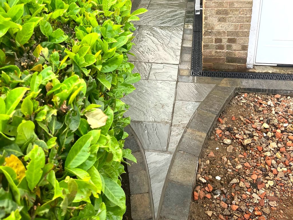 Sandstone side path running between a clipped hedge and a brick house
