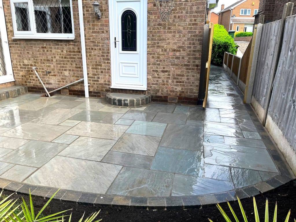 Sandstone patio wrapping the corner of a brick house with a curved sett edge