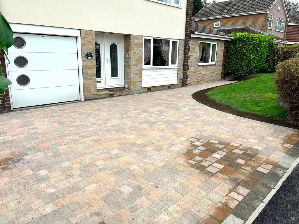 Block paved driveway sweeping up to a white garage door on a rendered house