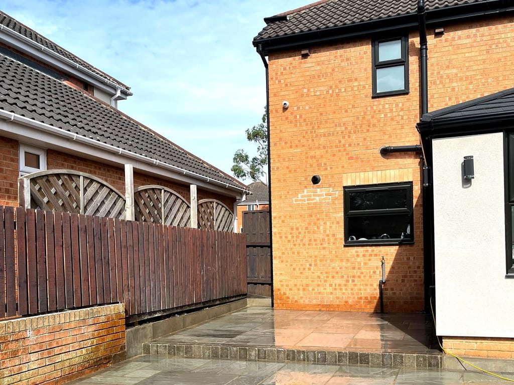 Sandstone patio at a brick house with a timber fence and lawn beyond