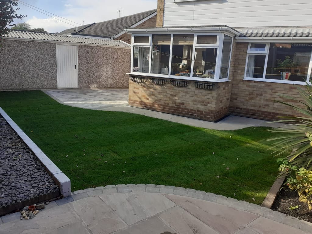 Lawn running up to a bungalow conservatory with sandstone paving at the near edge