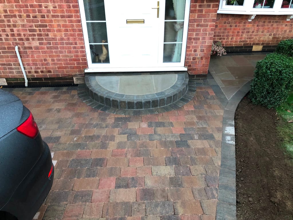 Block paved driveway in mixed brindle setts running up to a curved sandstone doorstep