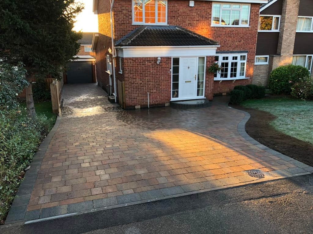 Wide block paved driveway with a curved lawn edge at a red brick semi with a white porch