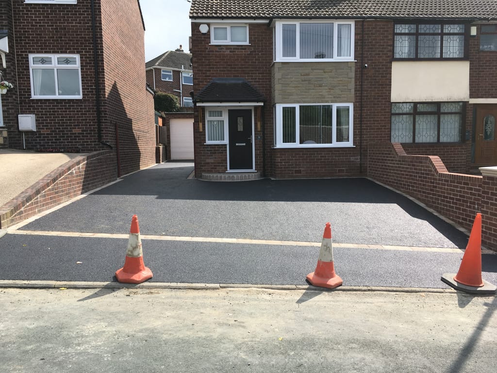Black tarmac driveway across the frontage of a brown brick semi with a bay window