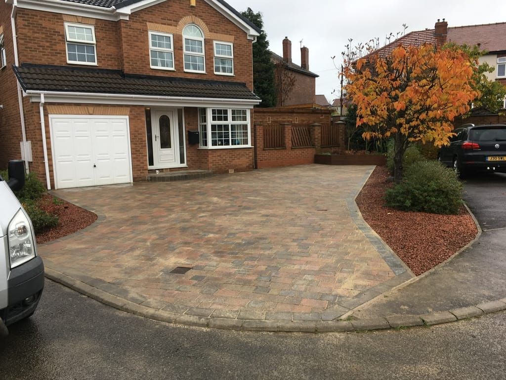 Large block paved driveway with a gravel border at a red brick house with an arched landing window