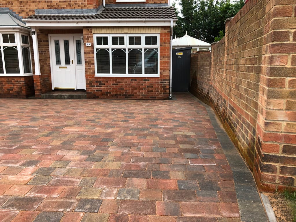 Brindle block driveway between a bungalow porch and a tall red brick boundary wall