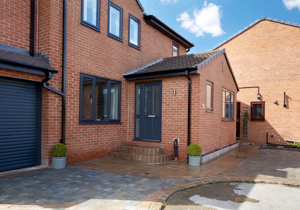 Sandstone and block paving at the anthracite front door of a modern red brick house