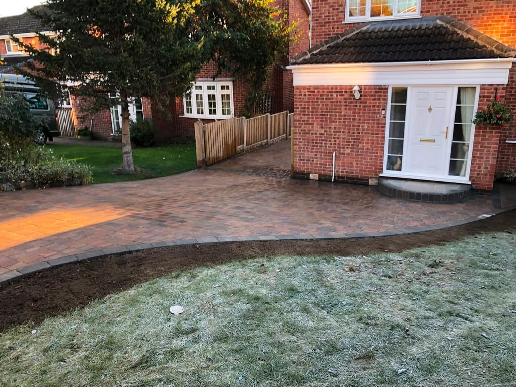 Curved block paved driveway past a frosted lawn and a mature tree to a white porch