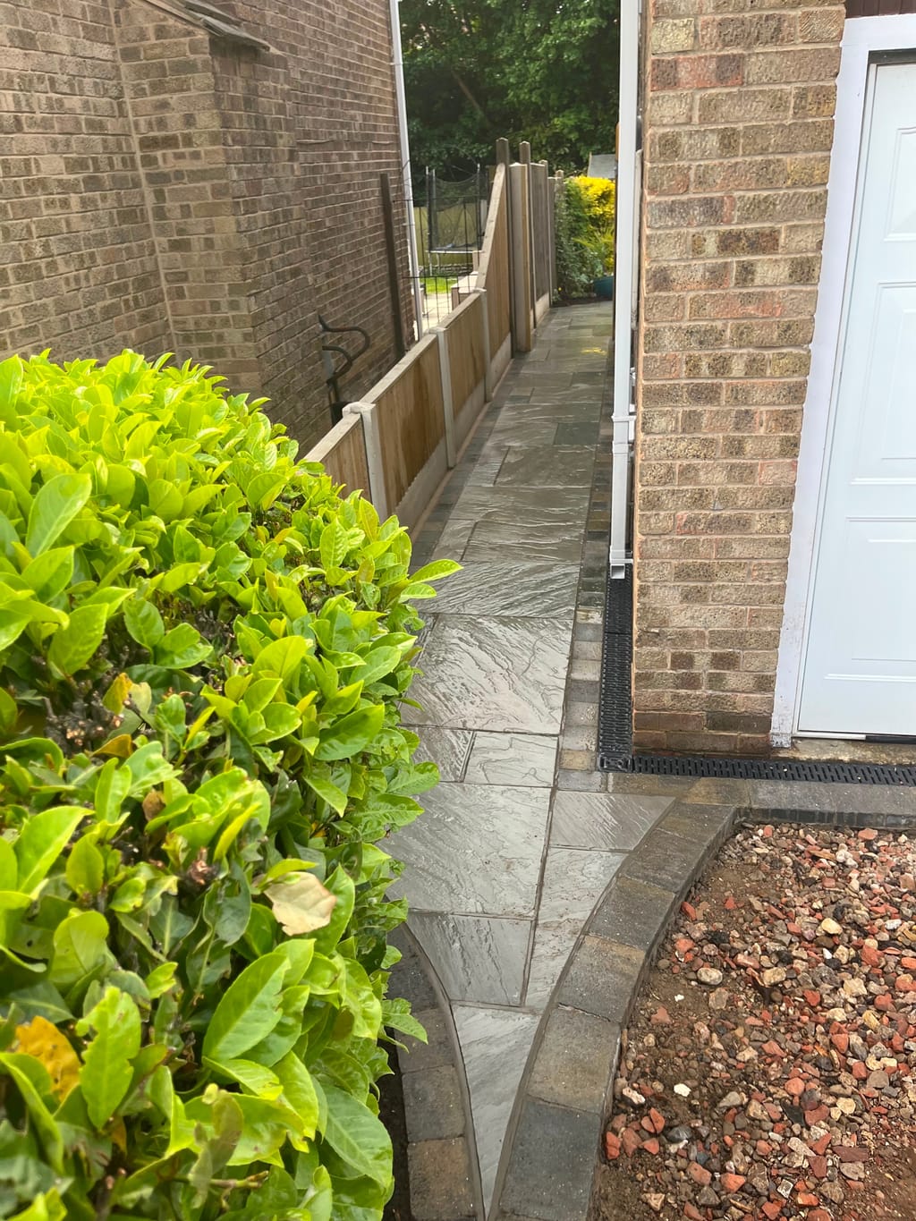 Sandstone side path with a sett border and a channel drain running past a laurel hedge