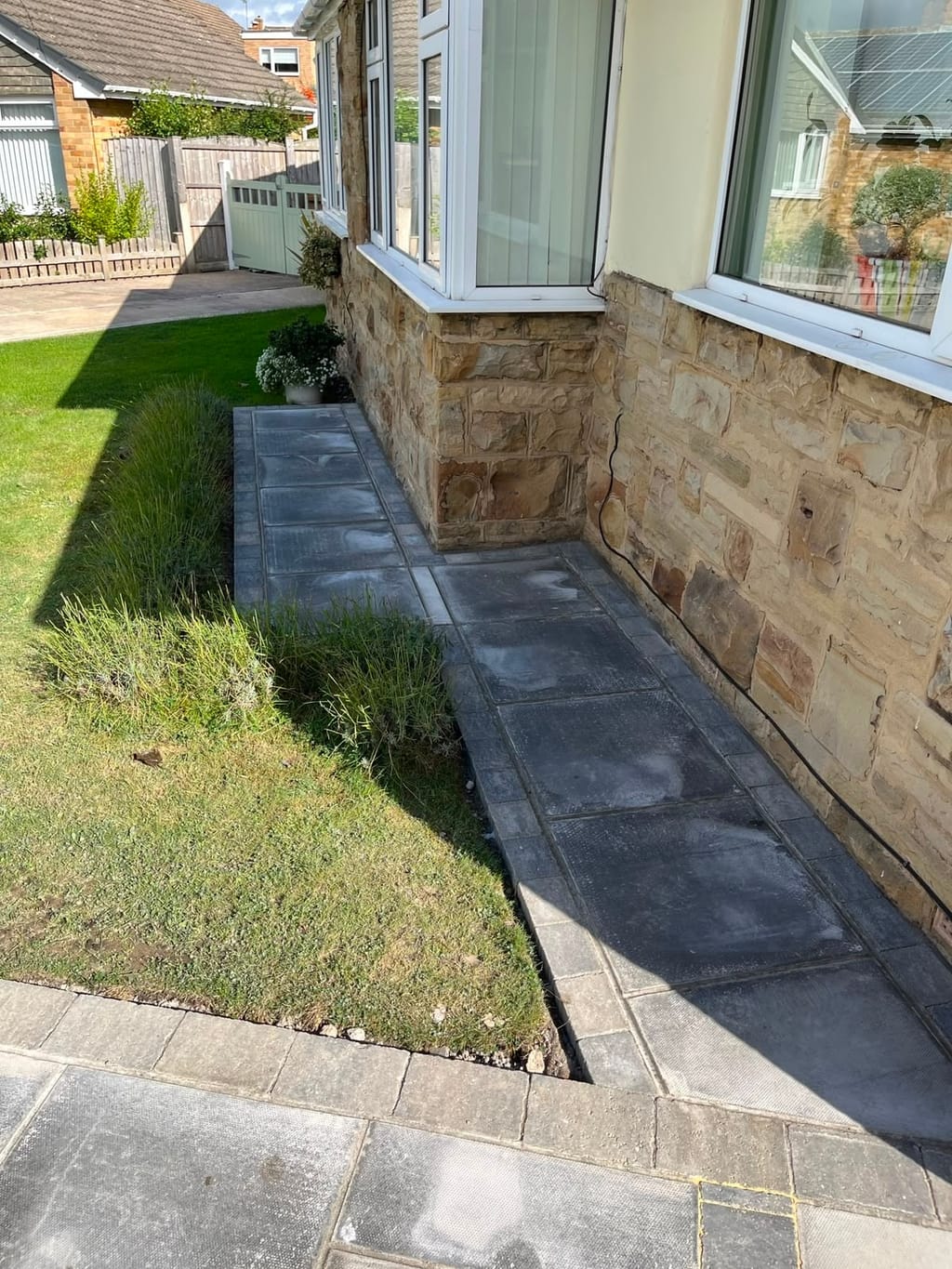 Dark slab path with a sett kerb along the stone front of a bungalow with bay windows