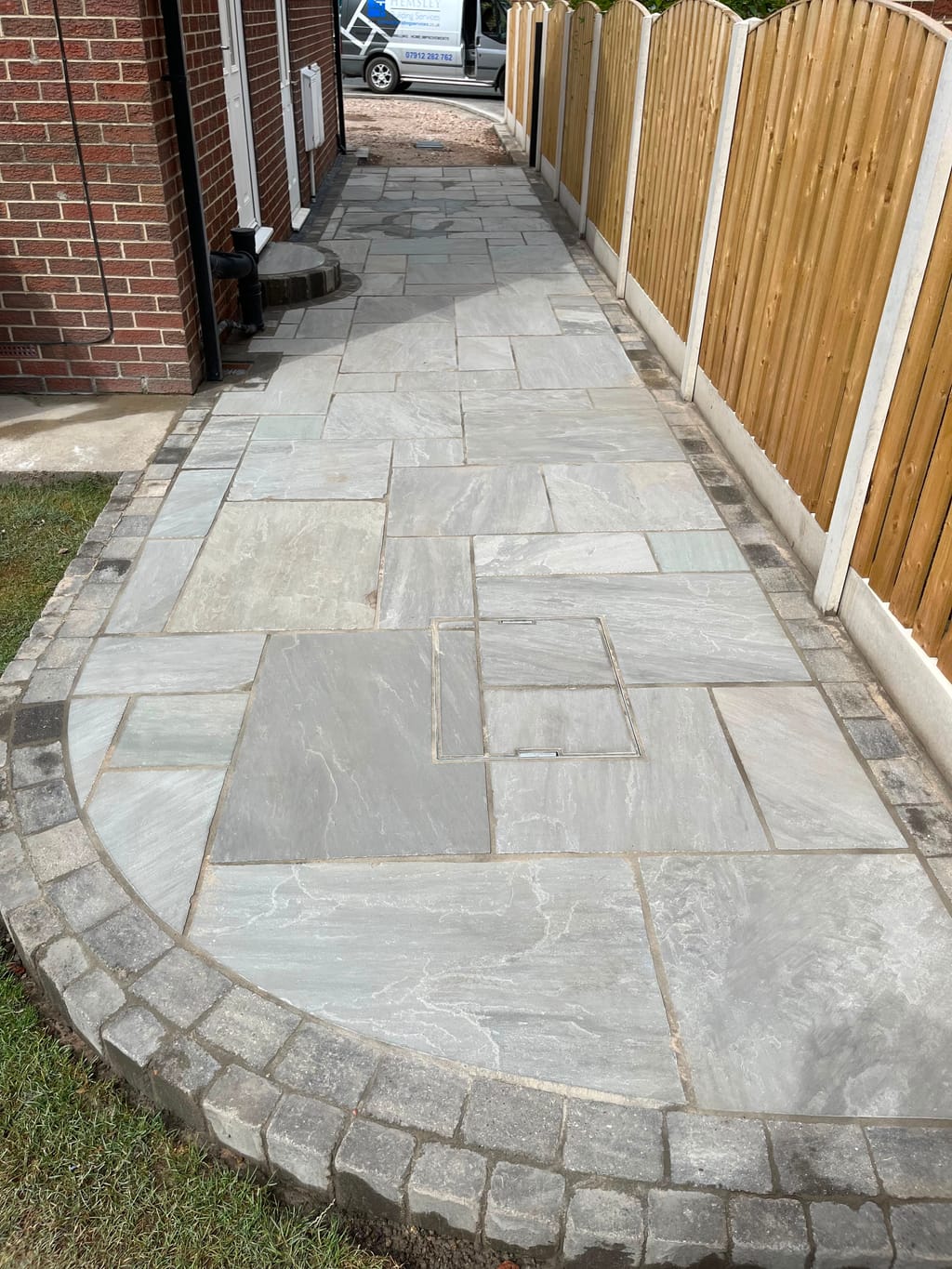 Grey sandstone path with a cobble edge curving to a point beside a close board fence