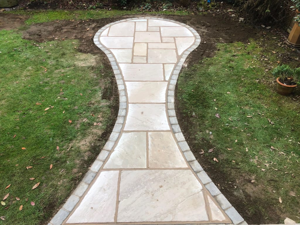 Cream sandstone path with a waisted shape and grey sett edging cut into a lawn