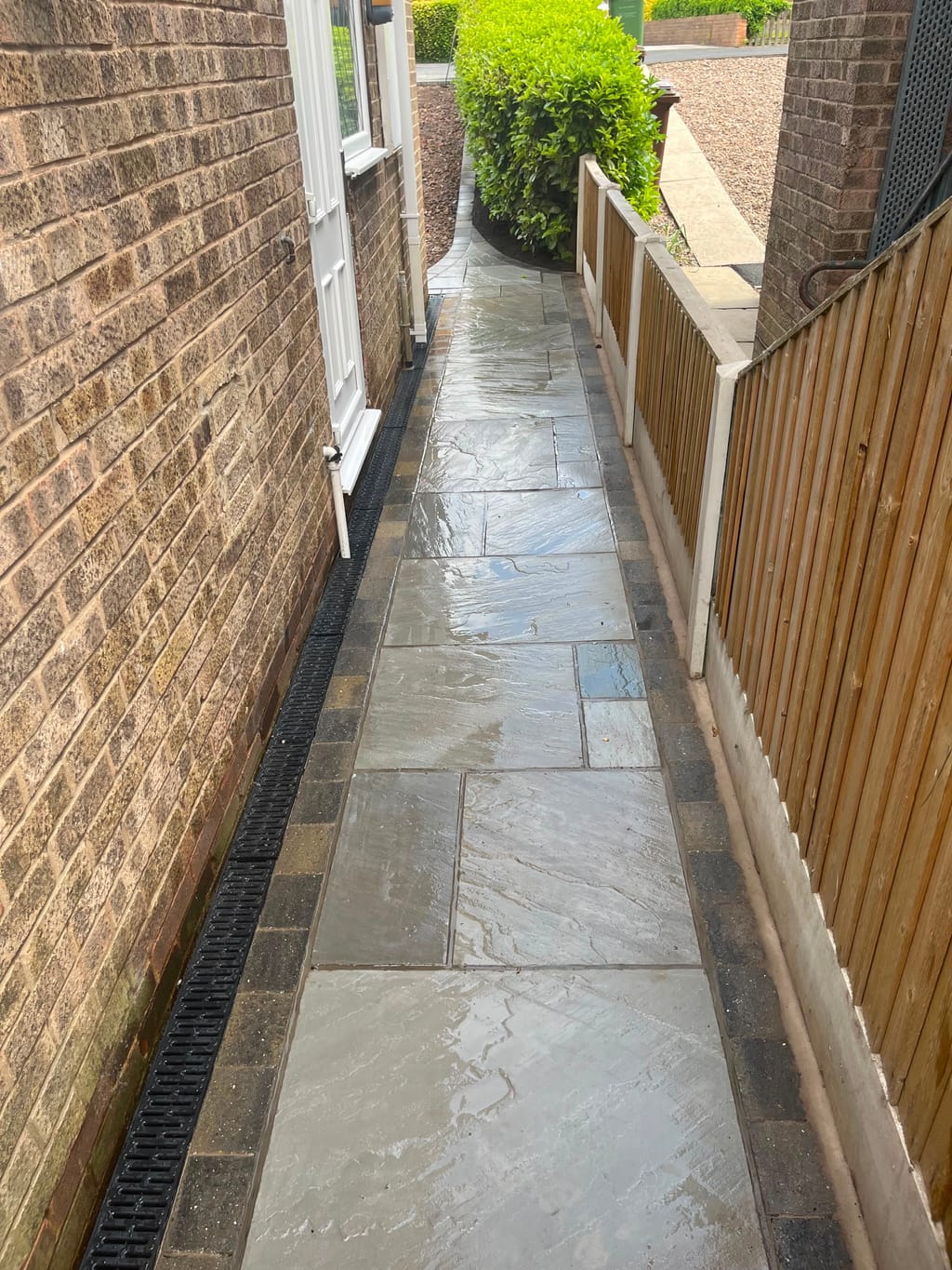 Wet grey sandstone side path with sett borders and a channel drain along the house wall