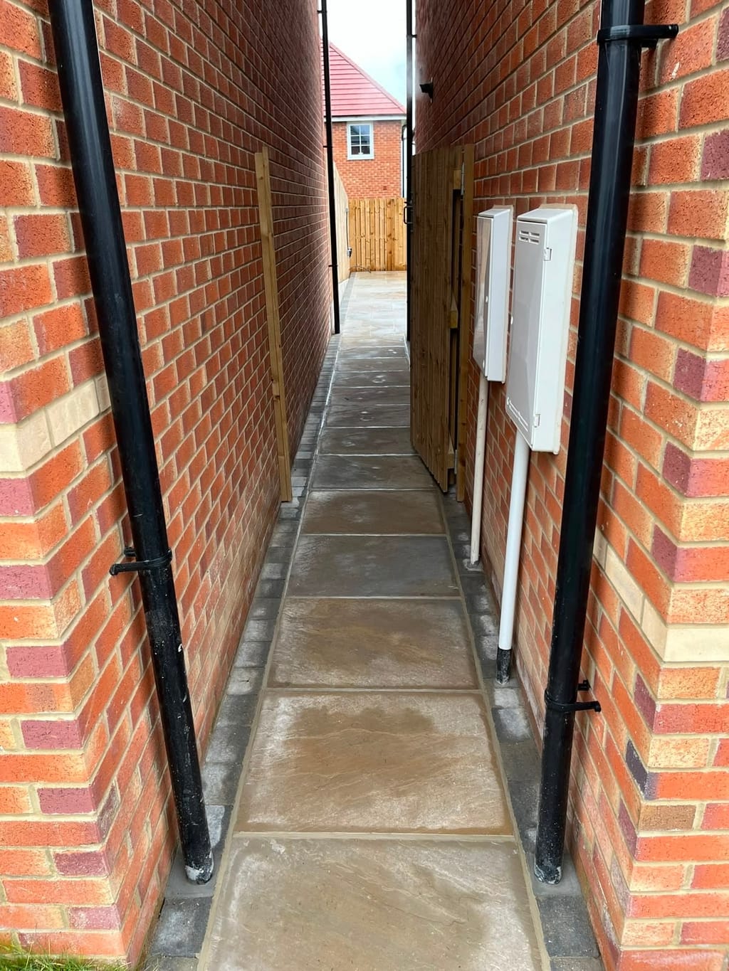 Sandstone path with a grey sett border running between two red brick walls
