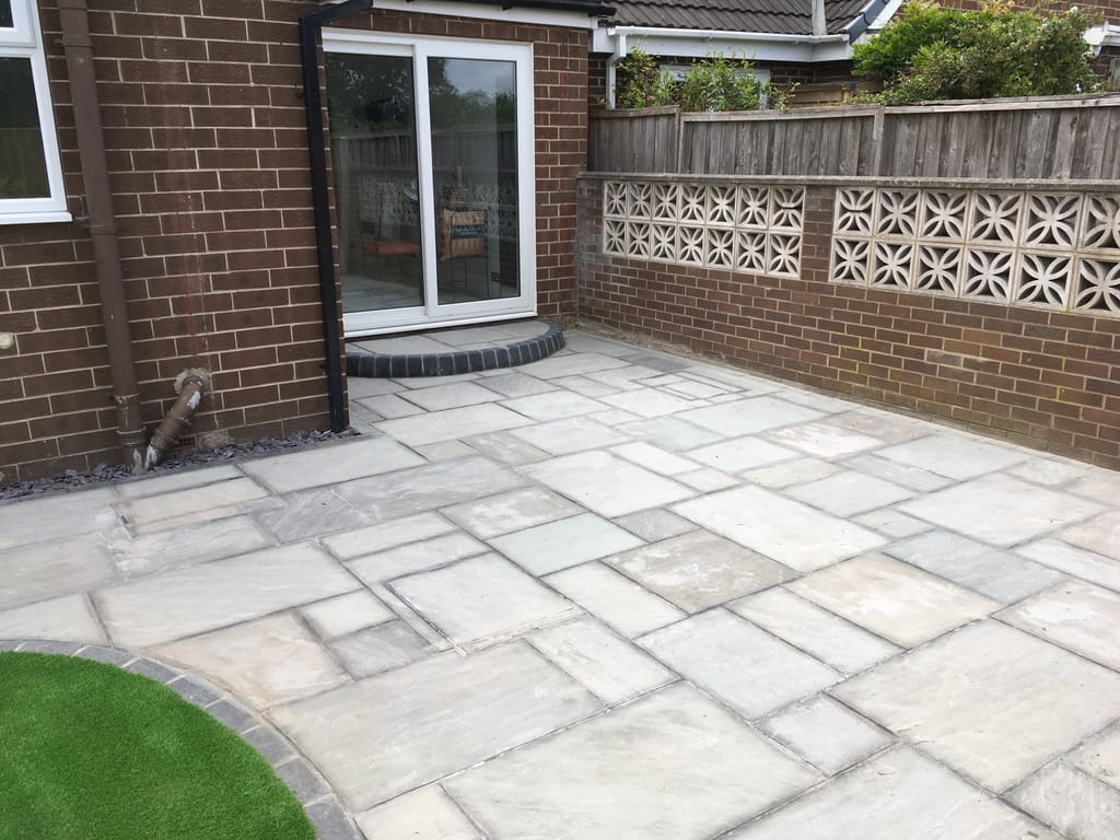 Grey sandstone patio with a curved sett step at the sliding doors of a brown brick bungalow