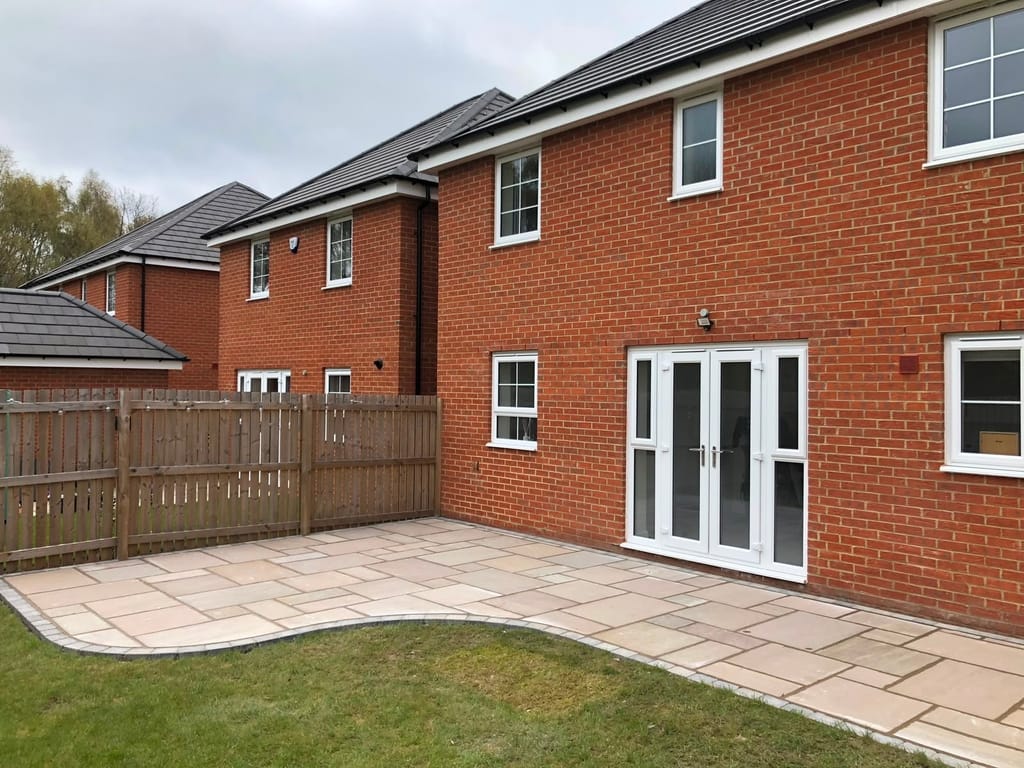 Slab patio with a curved edge onto the lawn behind a red brick house with white french doors
