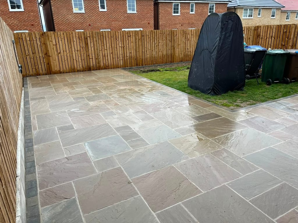 Wet sandstone patio with a charcoal sett border filling the rear garden of a new red brick house