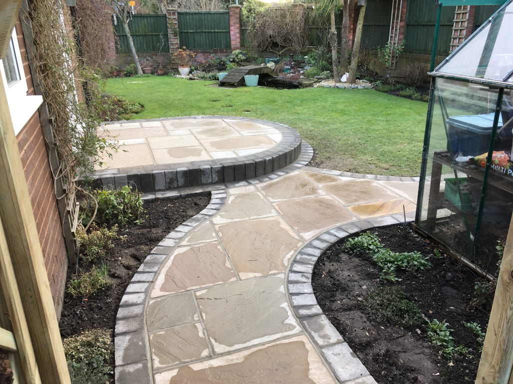 Circular sandstone patio and a curved linking path edged in charcoal setts beside a lawn
