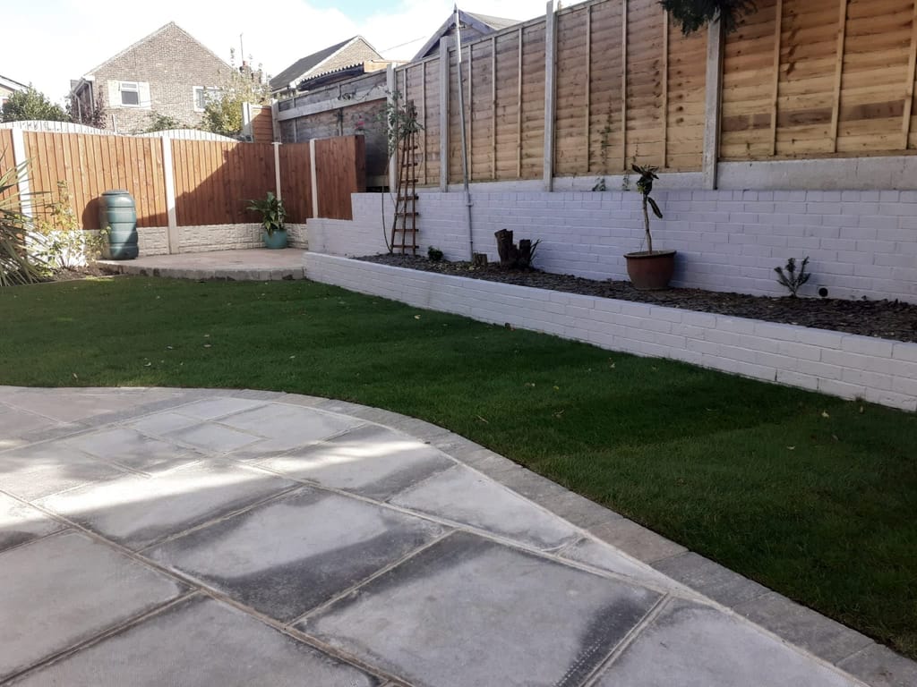 New lawn between a grey slab patio and a white painted brick retaining wall