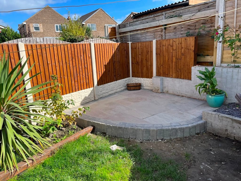 Corner patio with a curved sett edge set between painted block retaining walls and orange fence panels