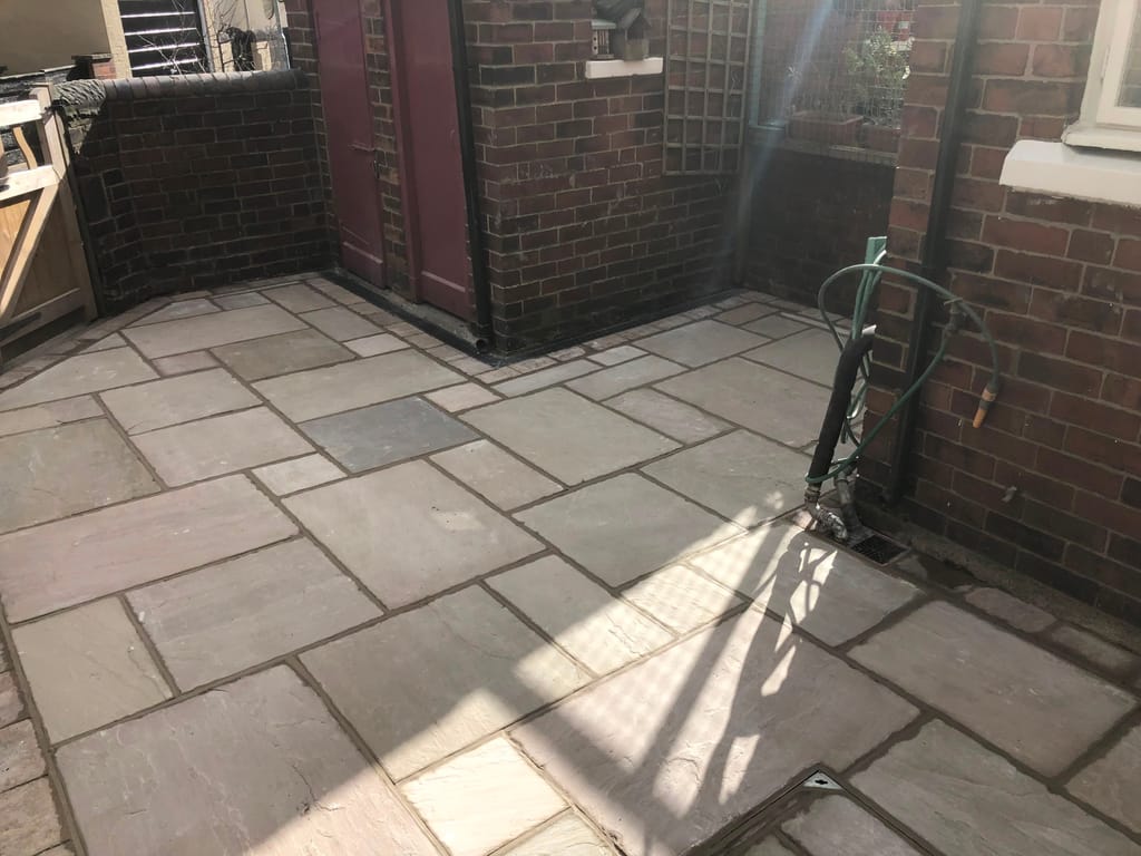 Grey sandstone paving filling an enclosed rear yard between red brick walls