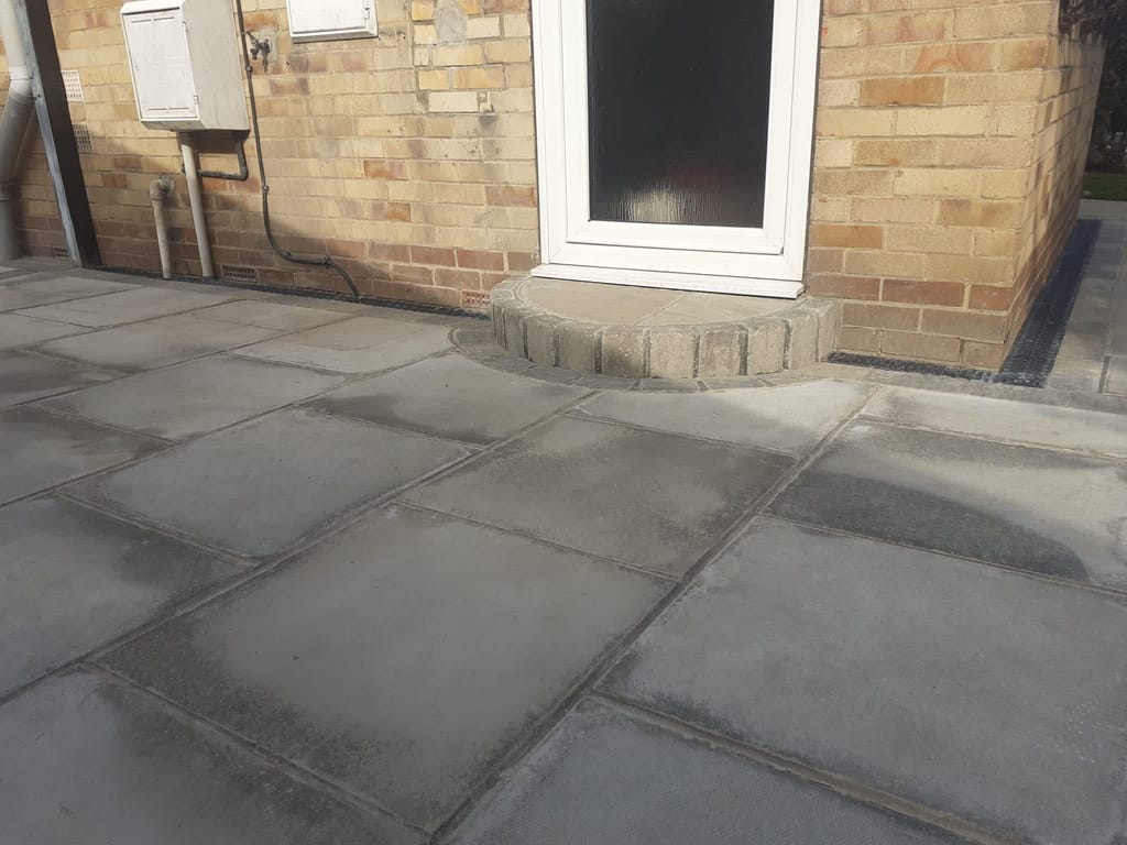 Large grey slabs with a curved sett step at the rear door of a buff brick house