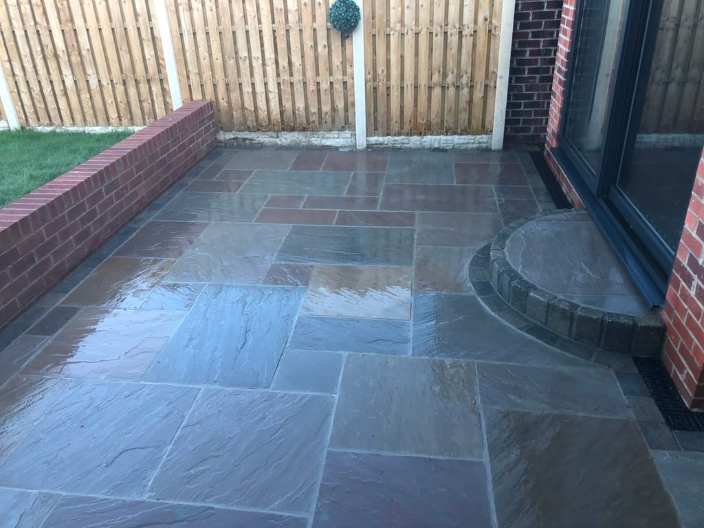 Sandstone patio with a curved sett step at black sliding doors and a low red brick wall