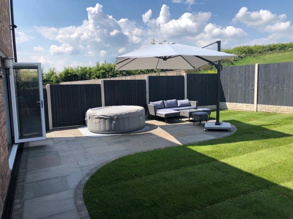Sandstone patio with a hot tub and a cantilever parasol beside a lawn and open countryside