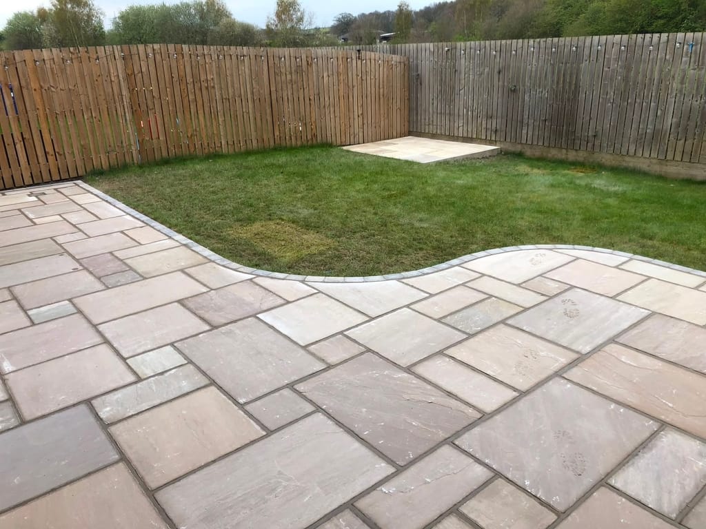 Sandstone patio with a long curved edge onto a lawn behind a close board fence