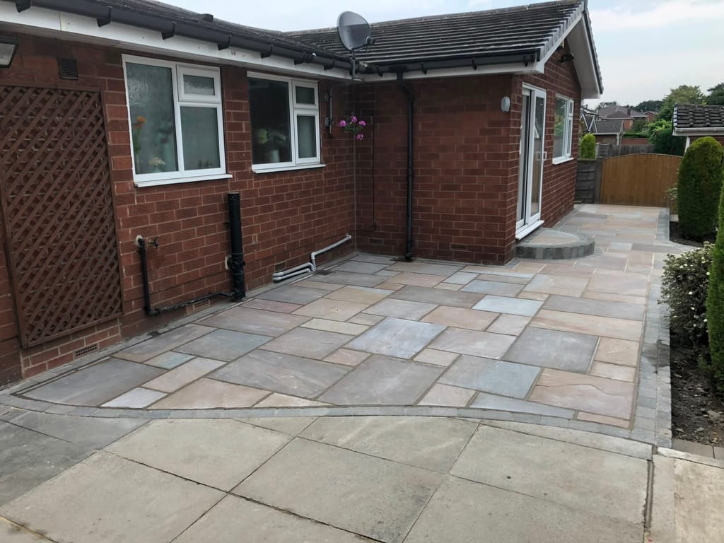 Sandstone patio wrapping the rear of a red brick bungalow with a lattice screen at one end