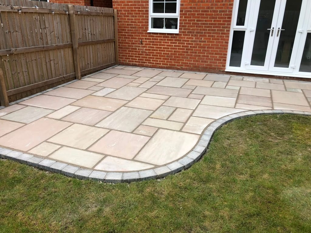 Sandstone patio with a charcoal sett kerb curving into the lawn at a red brick house