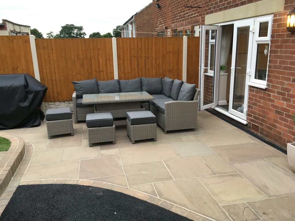 Sandstone patio with a slate border and a rattan corner sofa outside white french doors
