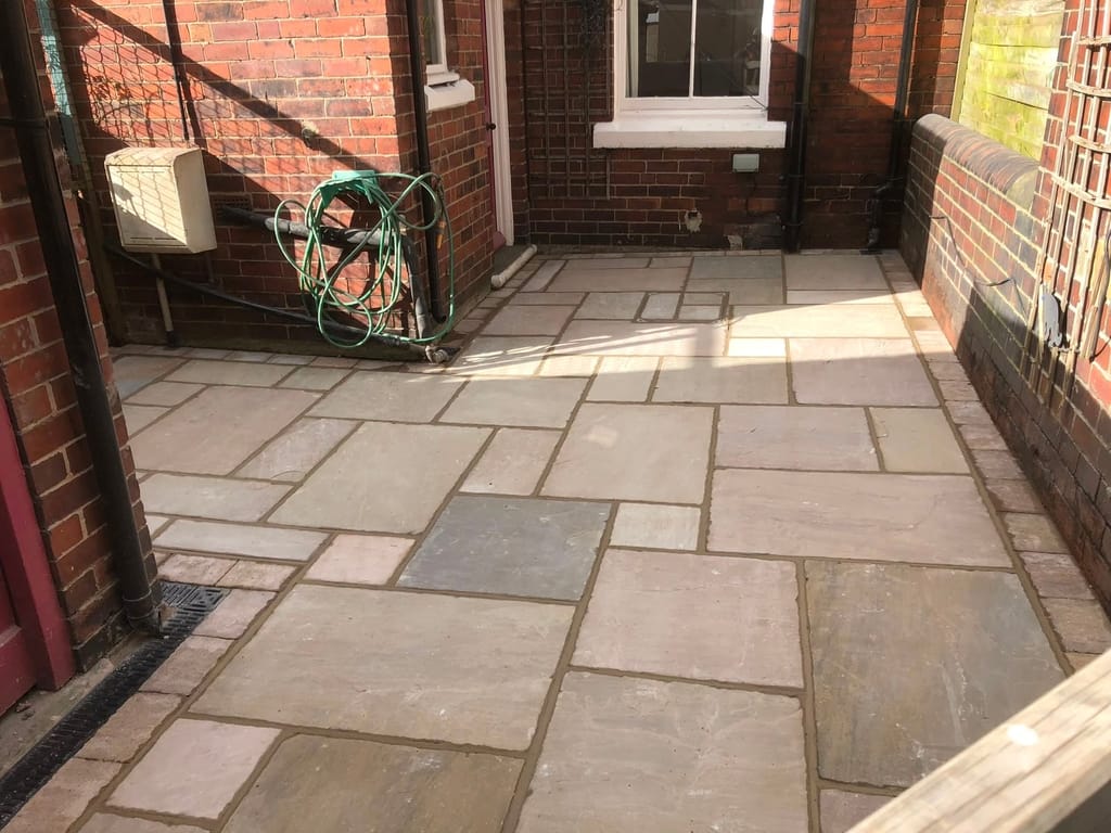 Sandstone paving in a narrow walled yard with a trellis panel on the boundary wall
