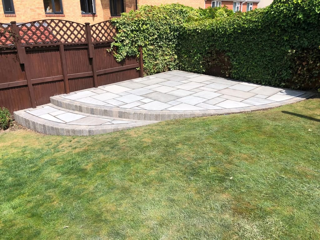 Raised sandstone patio with two curved sett edged steps down to a lawn