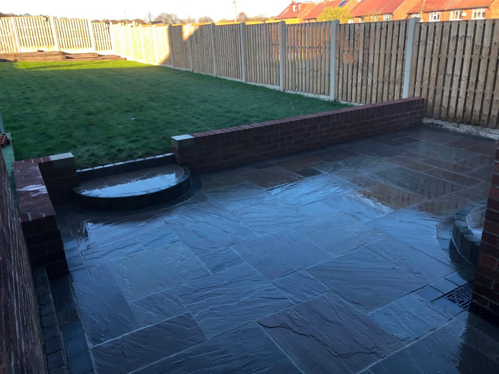 New red brick retaining walls with piers holding a raised lawn above a dark sandstone patio
