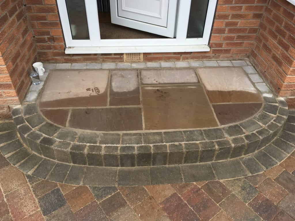 Curved sandstone doorstep with a charcoal sett riser at a white front door above block paving