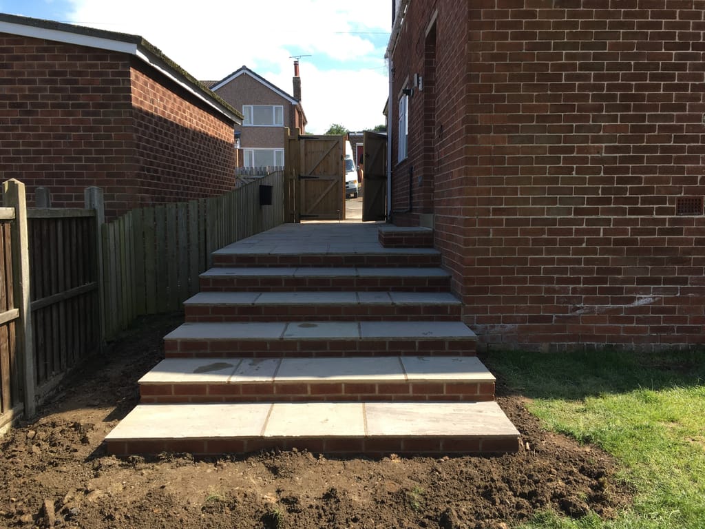 Flight of sandstone steps with red brick risers climbing a side passage beside a fence