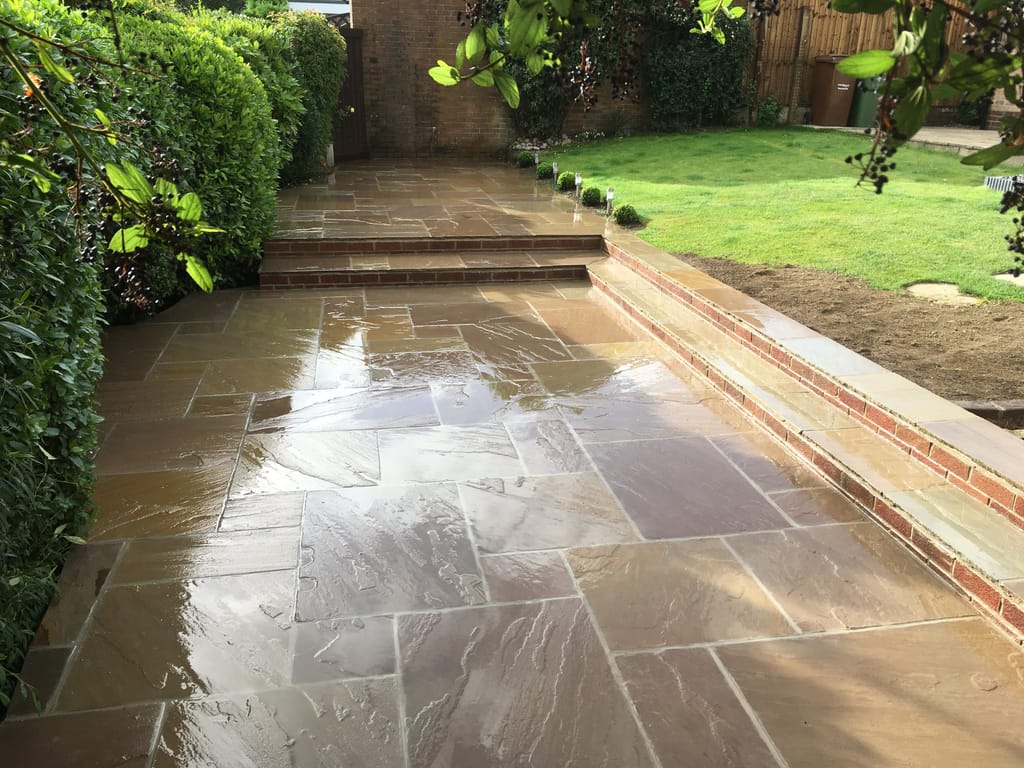 Wet sandstone terrace with brick faced steps rising to a lawn and a further path